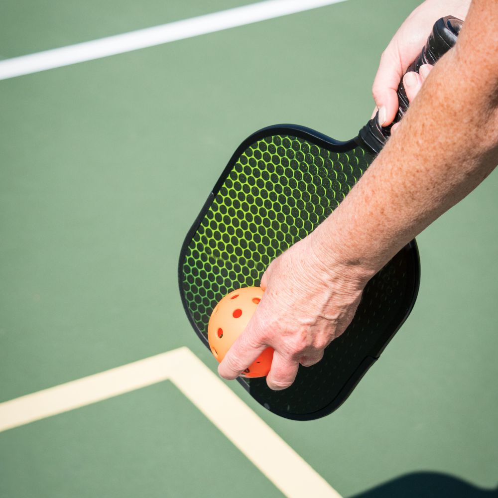 Foto van pickleballracket en pickleball bal, met hand van speler.